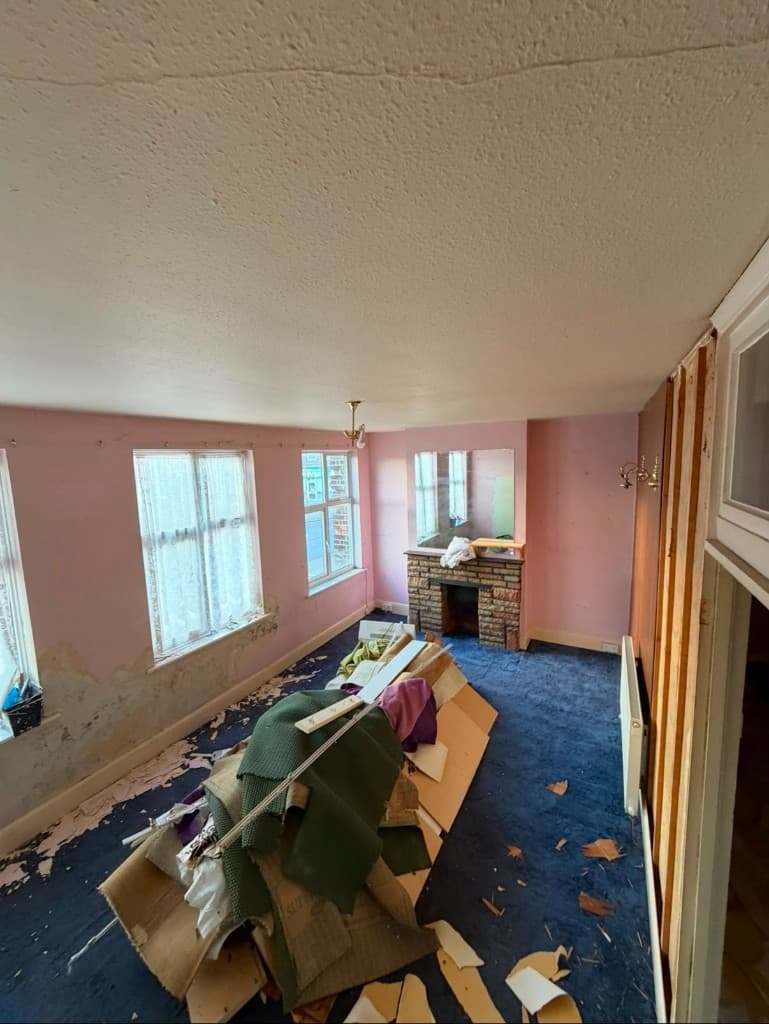 Living room before refurbishment, with worn carpet and stripped surfaces